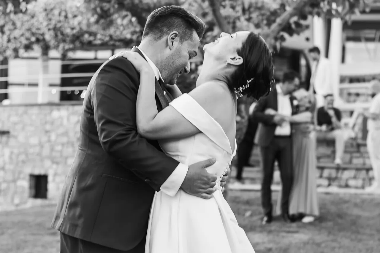 Laura and Davide laughing in an embrace, in black and white