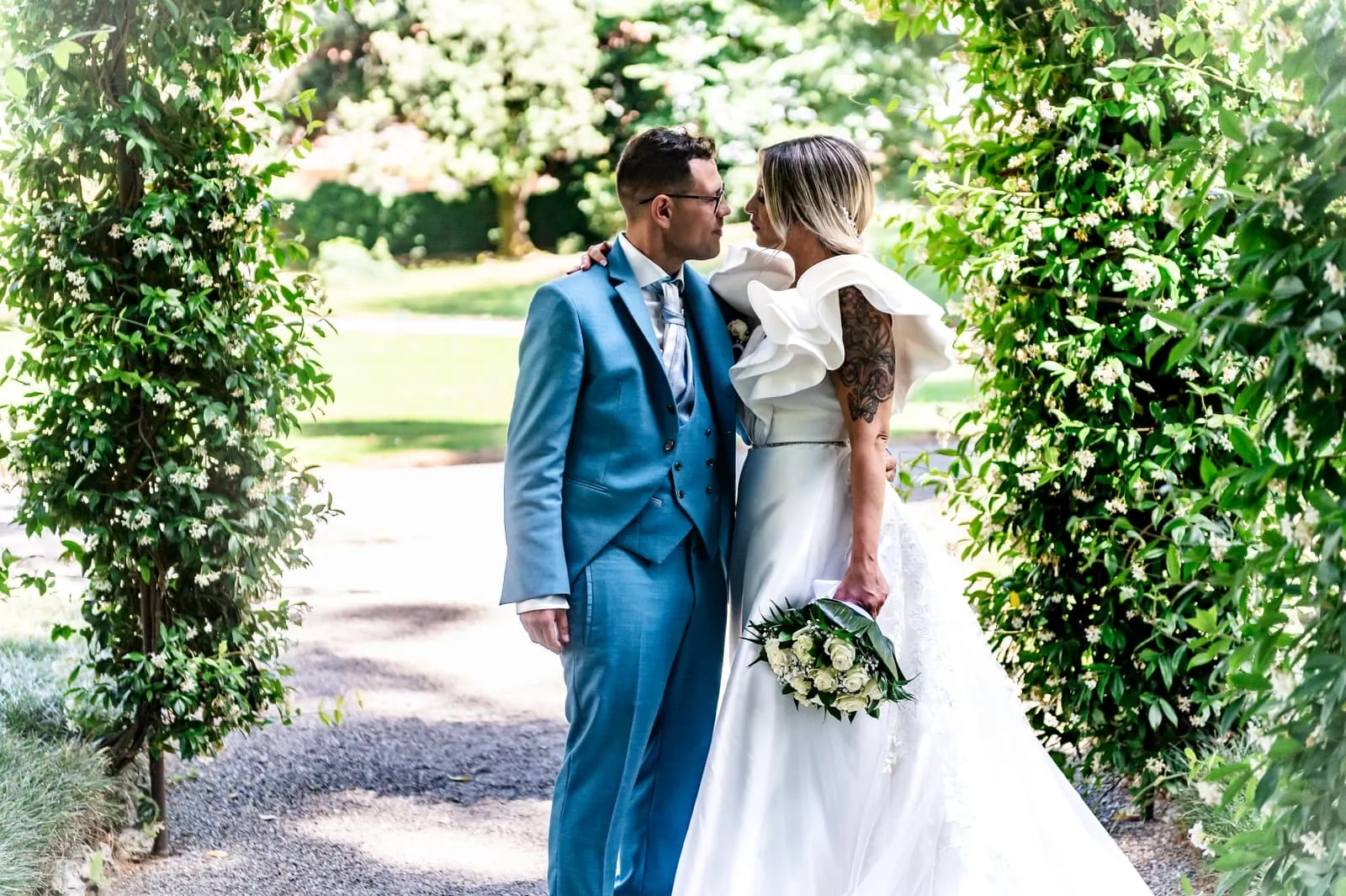 Nikla and Maurizio leaning towards each other beneath an arch of leaves