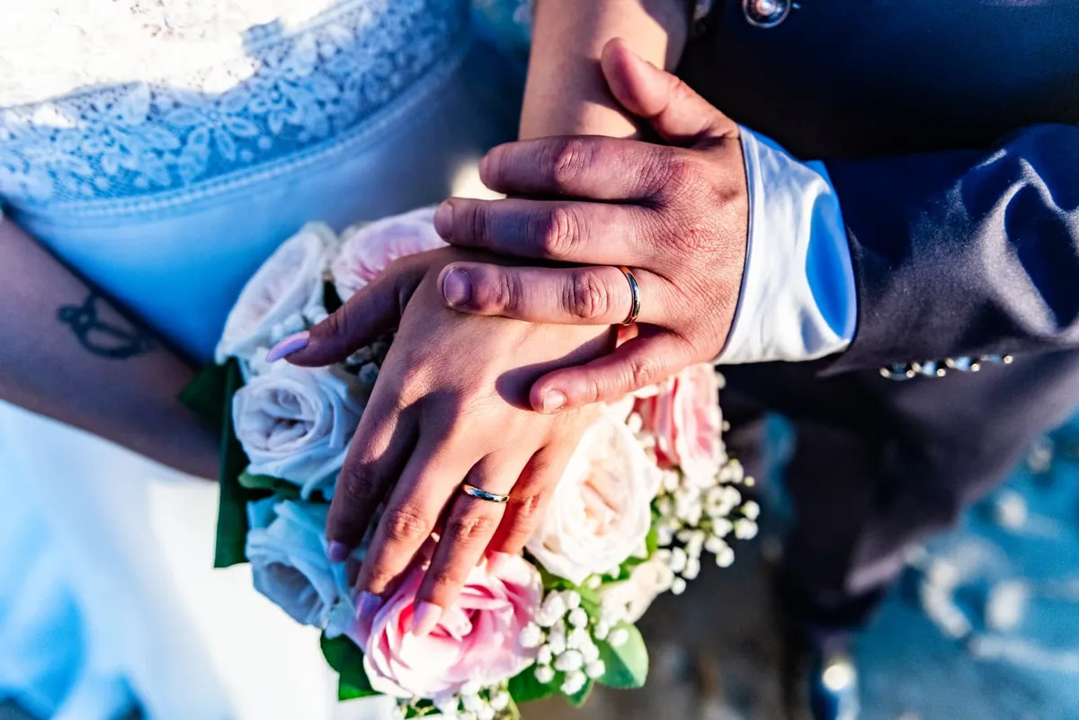 Le mani e le fedi di Valentina e Christian sul bouquet