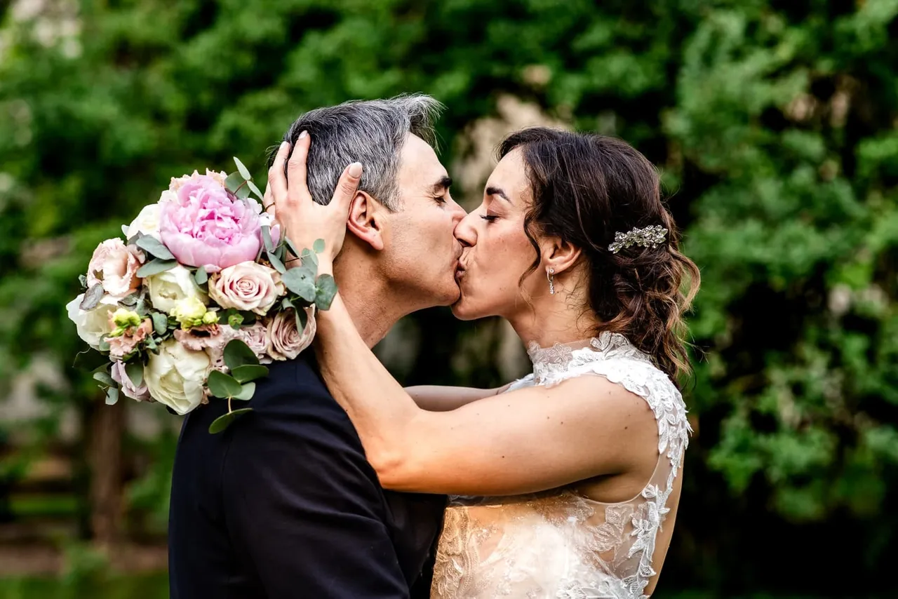 Veronica and Carlo kissing with the pink bouquet beside their faces