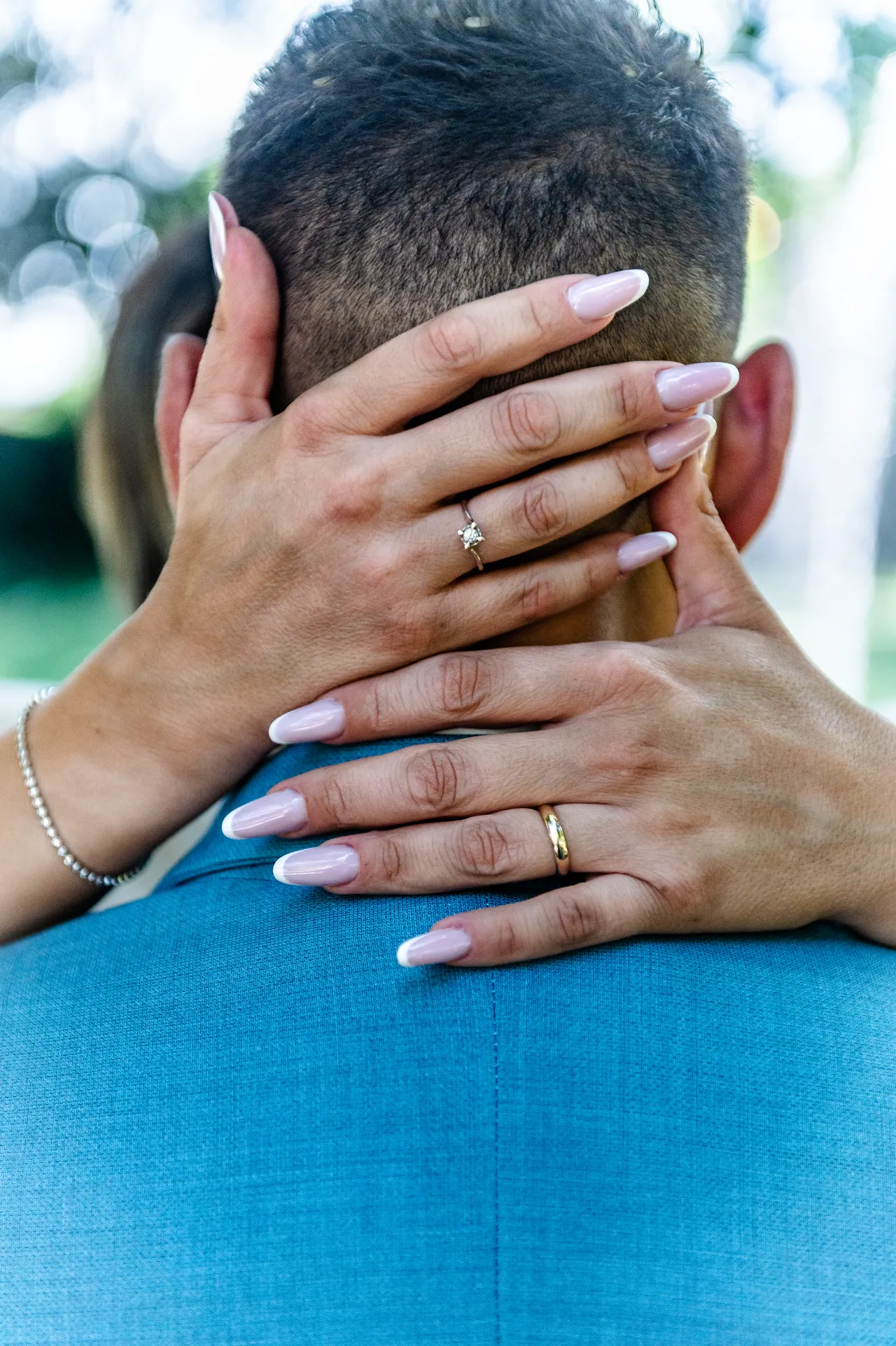 Le fedi sulle mani della sposa appoggiate al collo dello sposo