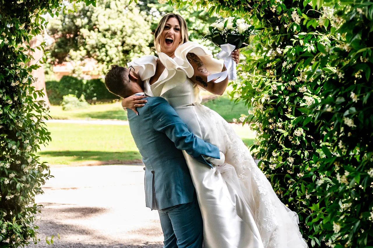 Lo sposo porta la sposa in braccio tra il verde